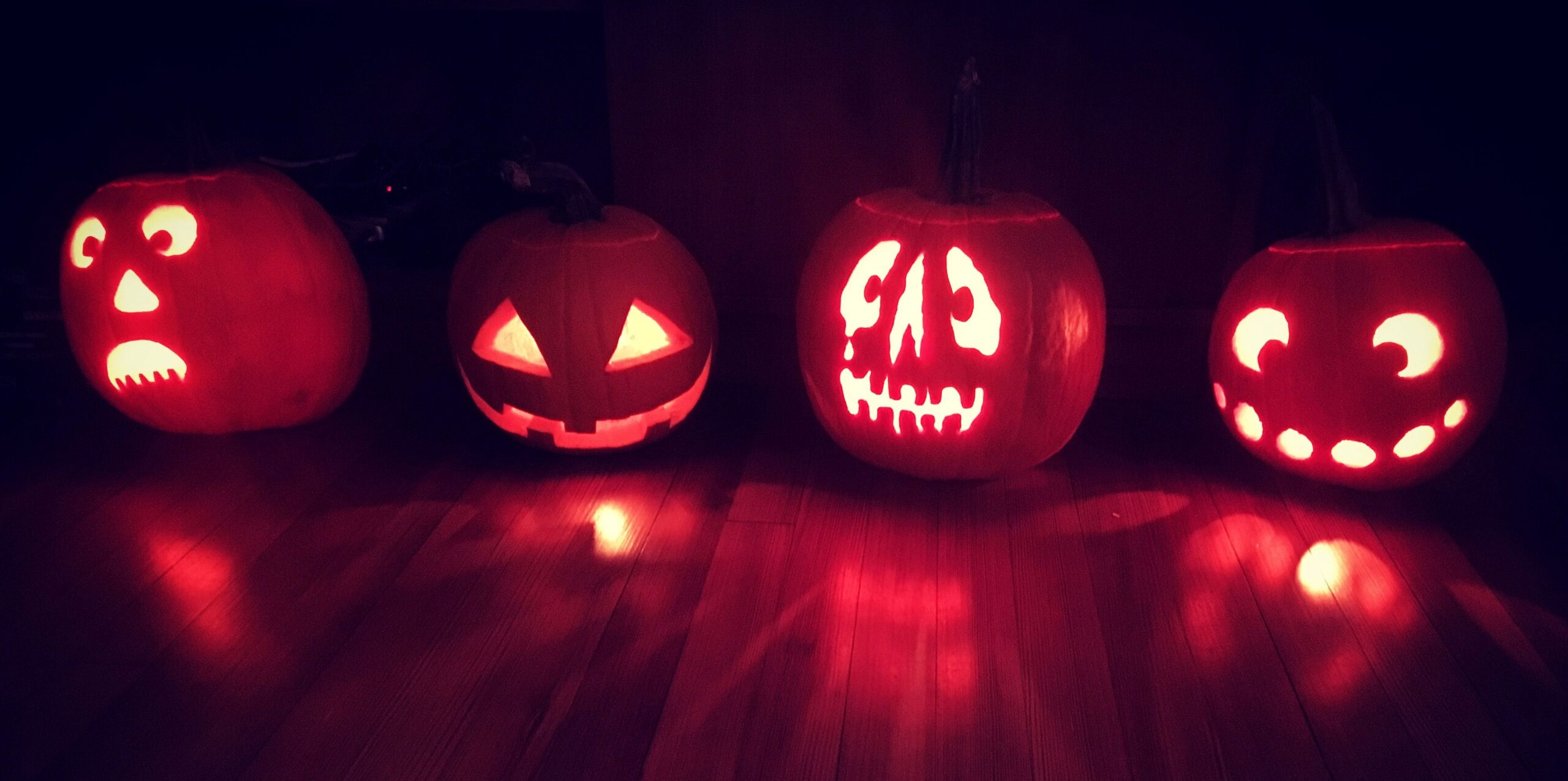 four carved jack o lanters on a wood floor with four different faces, lit up at night